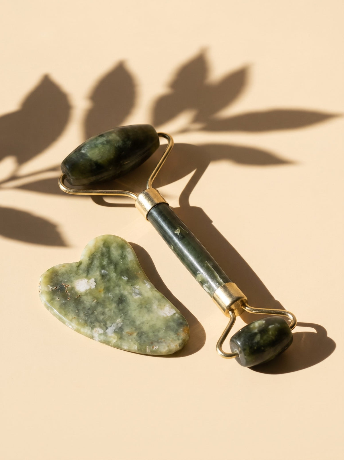 Rodillo y piedra gua sha de jade verde, sobre fondo melocotón con sombras de hojas