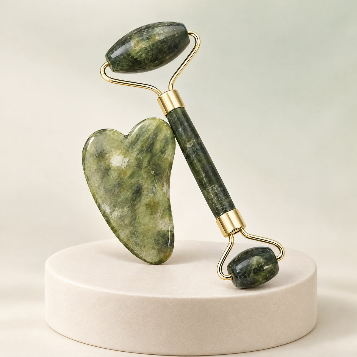 Rodillo facial y piedra gua sha de jade verde apoyados en un pedestal claro