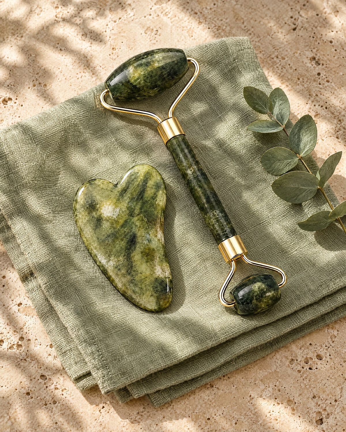 Rodillo y piedra gua sha de jade sobre un paño de lino verde con eucalipto