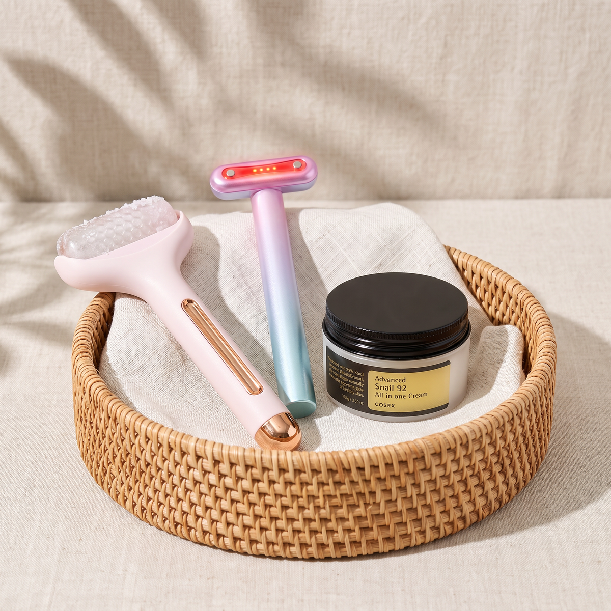 Rodillo facial frío Escarcha, varita Aurora y crema COSRX Advanced Snail 92 en una cesta de ratán